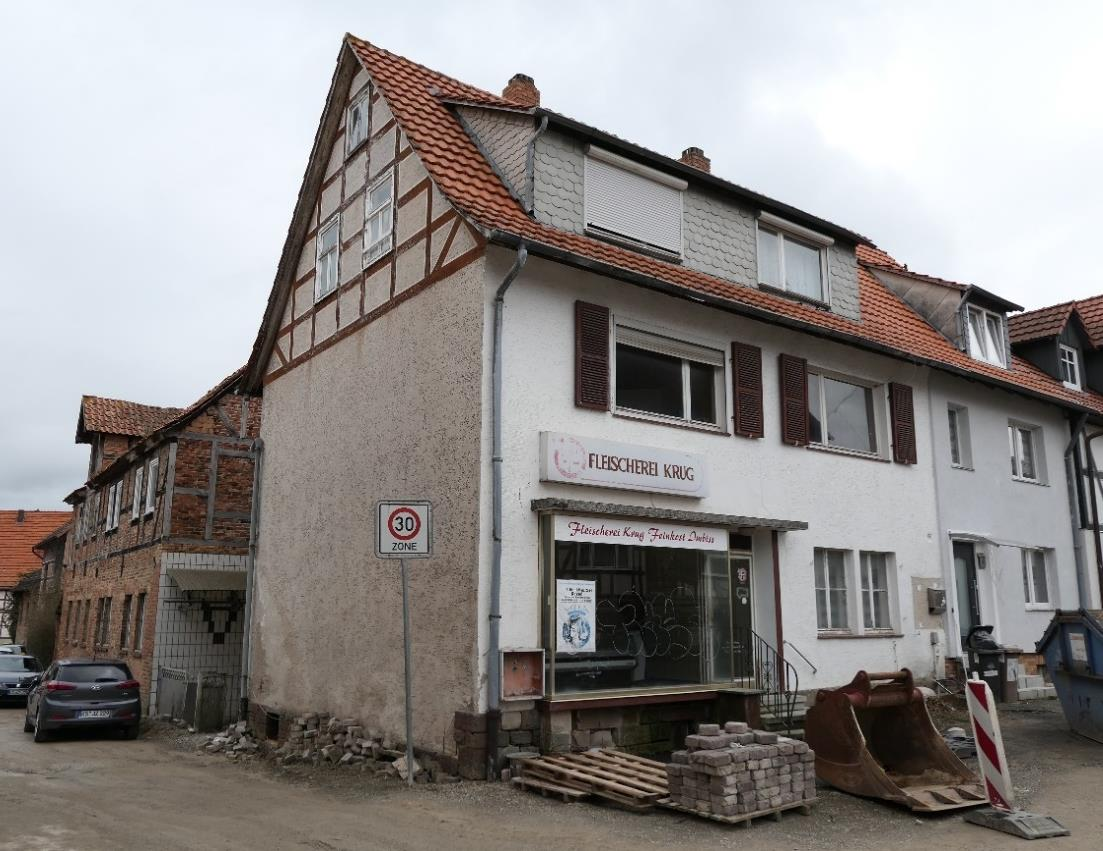 Einfamilienhaus mit Fachwerkdetails und Ladenlokal Fleischerei Krug, Wilhelmsthaler Straße 23, Calden, mit rotem Ziegeldach und Baustellenmaterial vorne
