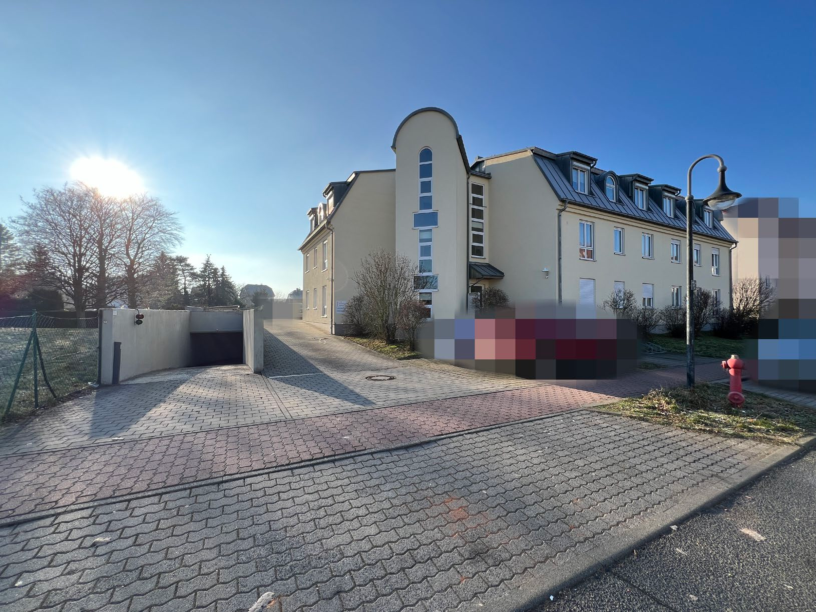 Außenansicht vorne eines mehrstöckigen Wohngebäudes in Borsdorf, An der Parthenaue 1, mit gepflastertem Vorplatz und Sonneneinstrahlung von links