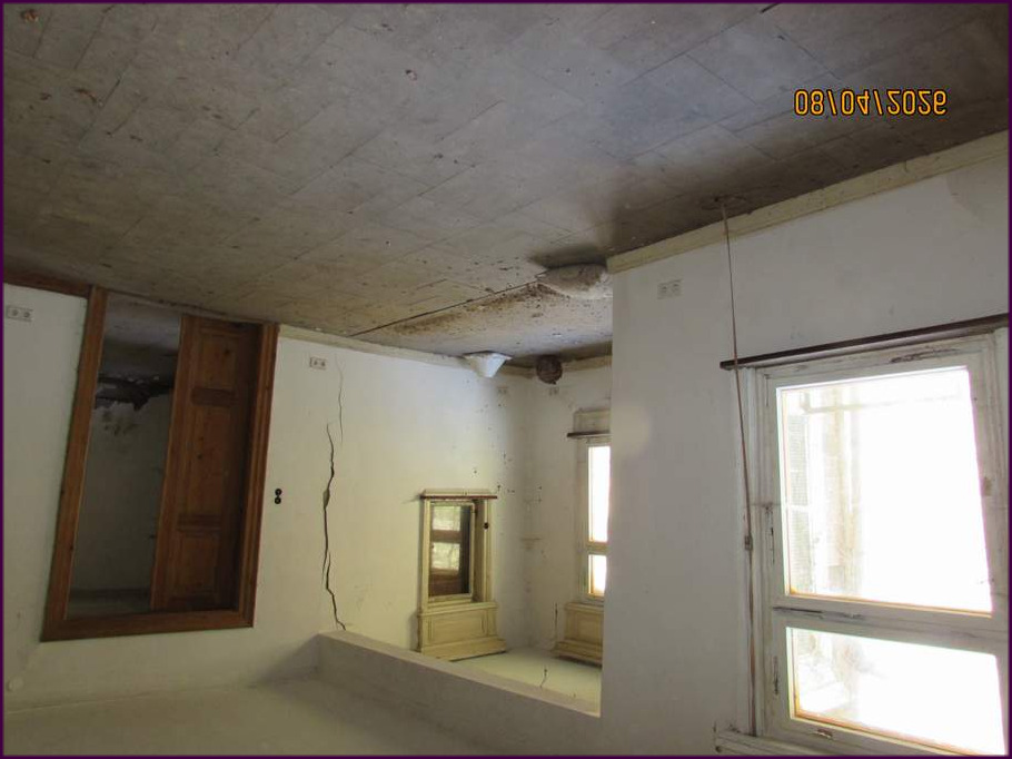 Innenraum eines Einfamilienhauses mit sichtbaren Rissen in Wand und Decke, alten Holztüren und Fenstern, sowie einem veralteten Schrank