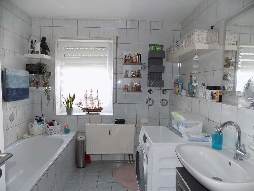 Badezimmer mit Badewanne, Waschbecken, Waschmaschine und Fliesenwand, Fenster mit Blick nach draußen, dekorative Gegenstände und Regale