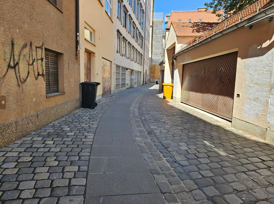 Schmale gepflasterte Gasse mit Gebäuden an beiden Seiten, darunter eine Garagentür und Fenster, im Stadtteil Augsburg