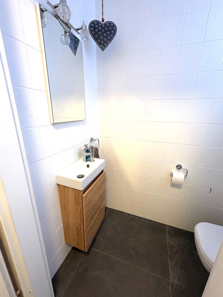 Badezimmer mit weiß gefliesten Wänden, Holzwaschtisch, Spiegel und Toilettenpapierhalter