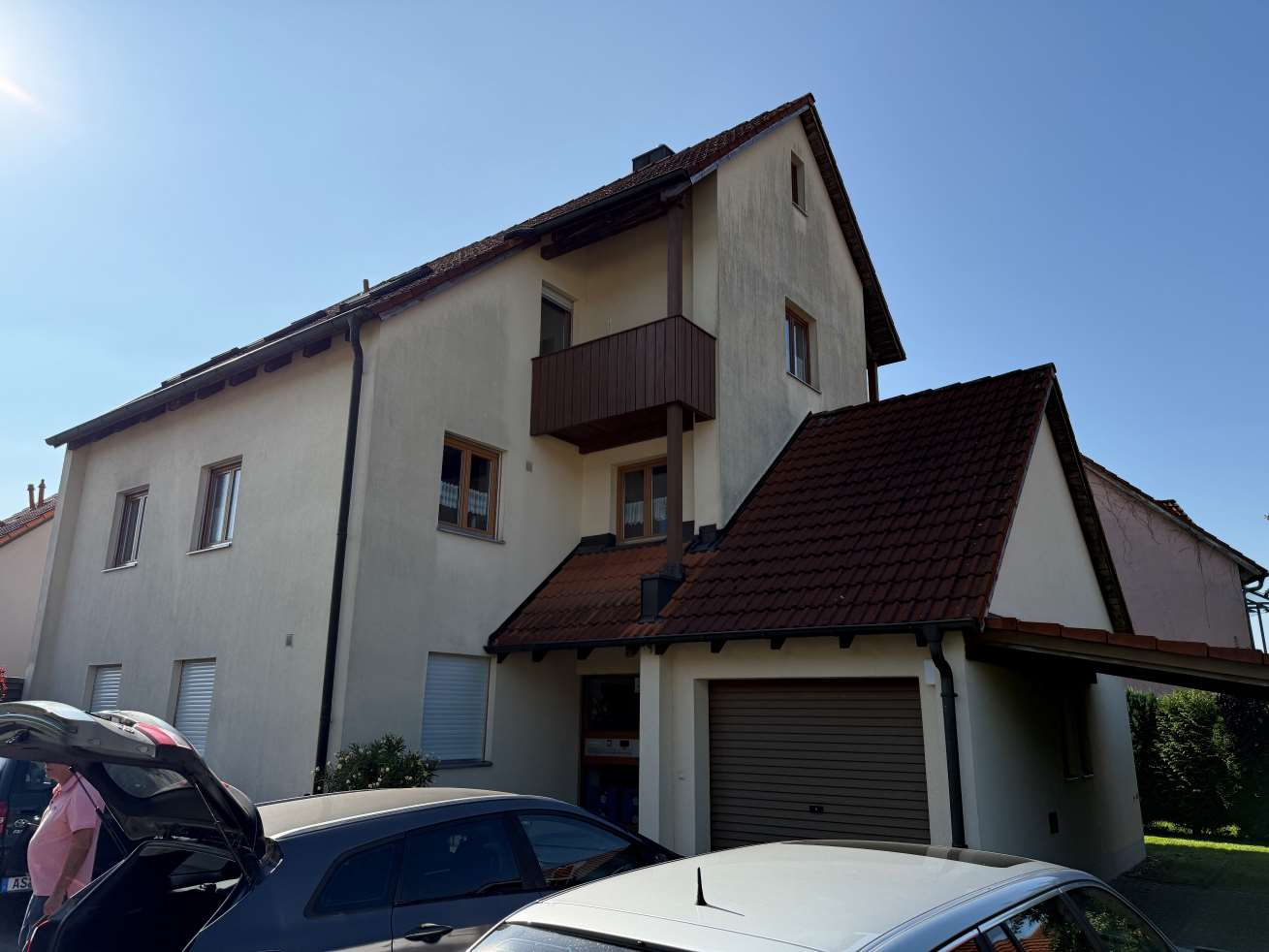 Fassade eines zweistöckigen Wohnhauses mit Balkon, Garagenstellplatz und Satteldach unter klarem Himmel