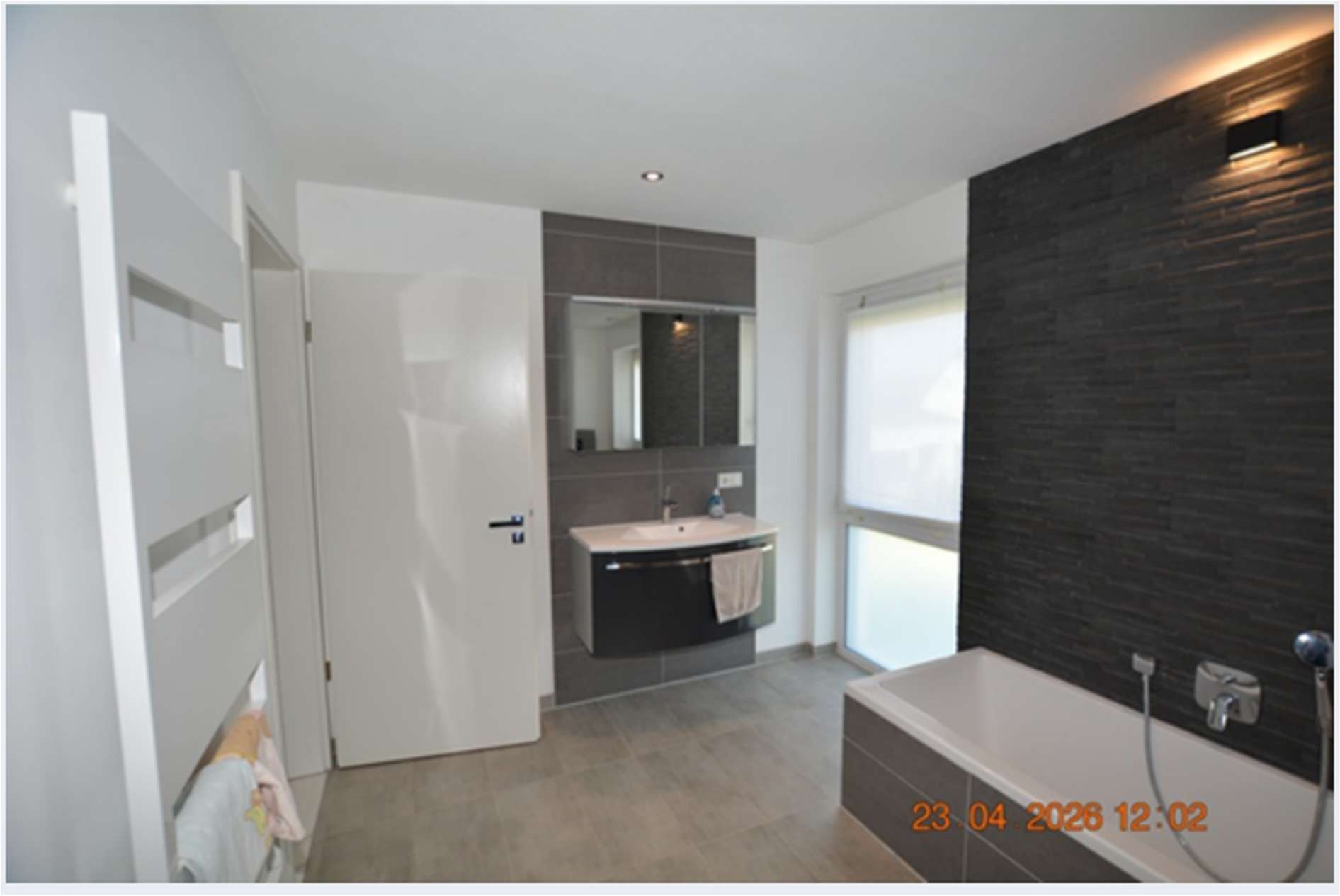Modernes Badezimmer mit Badewanne, Waschtisch, Spiegel und dunklen Wandfliesen im Einfamilienhaus Volgersweg 1, Laatzen