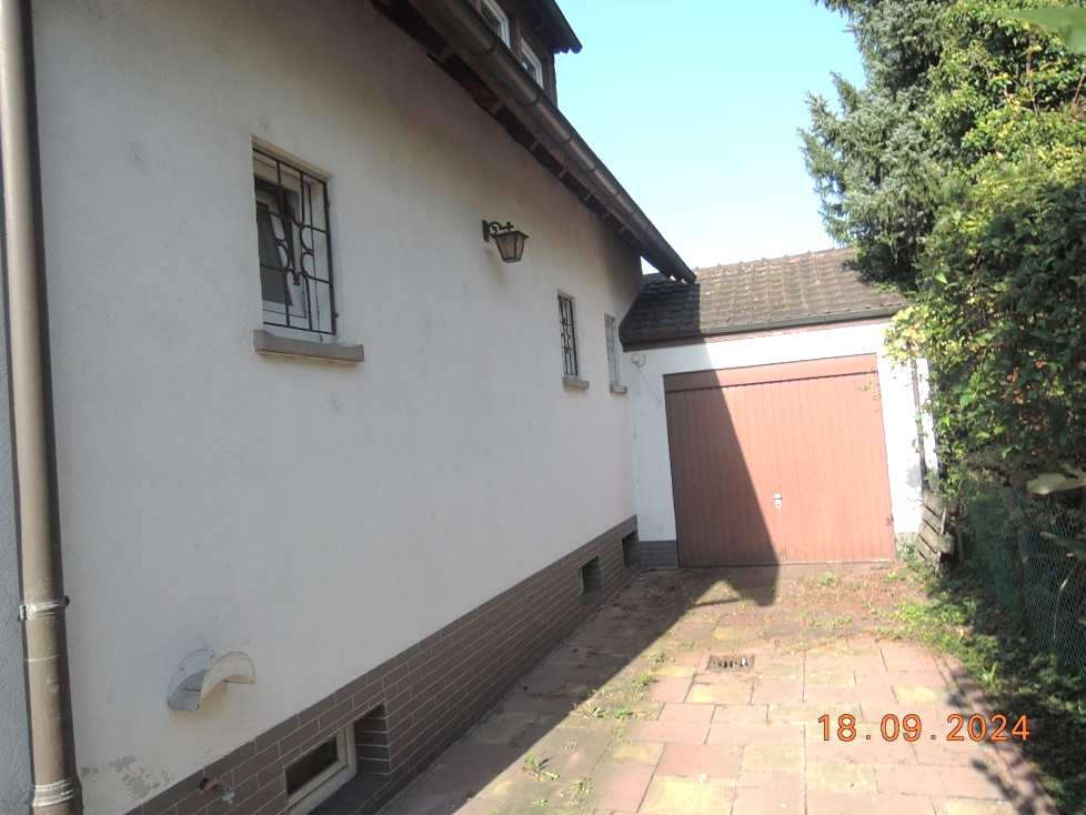 Seitenansicht eines Gebäudes mit weißer Fassade, Fenstern mit Gitter, Wandlampe und angrenzender Garage mit brauner Tür in Limburgerhof, Feuerbachstraße 23