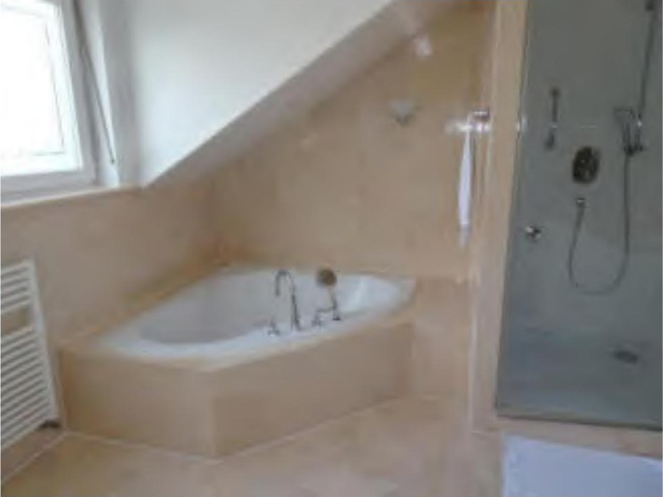 Badezimmer mit Badewanne und Dusche unter schräger Decke, beige Fliesenverkleidung, Fenster links