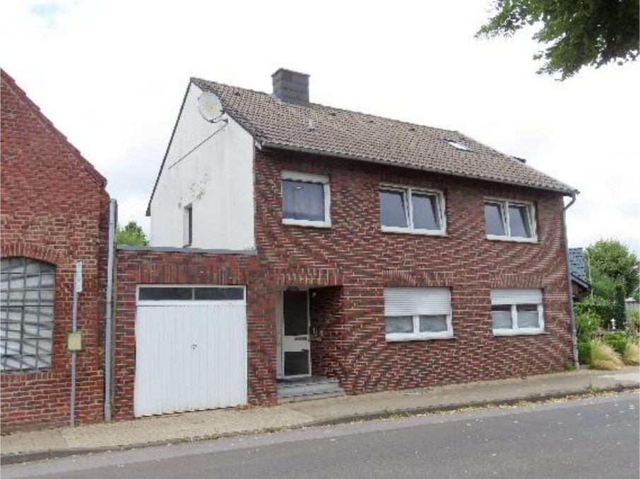 Einfamilienhaus in Titz, Bachstraße 18, mit rotem Backsteinfassade, Eingangstür, Garagentor und Dach mit Satellitenschüssel