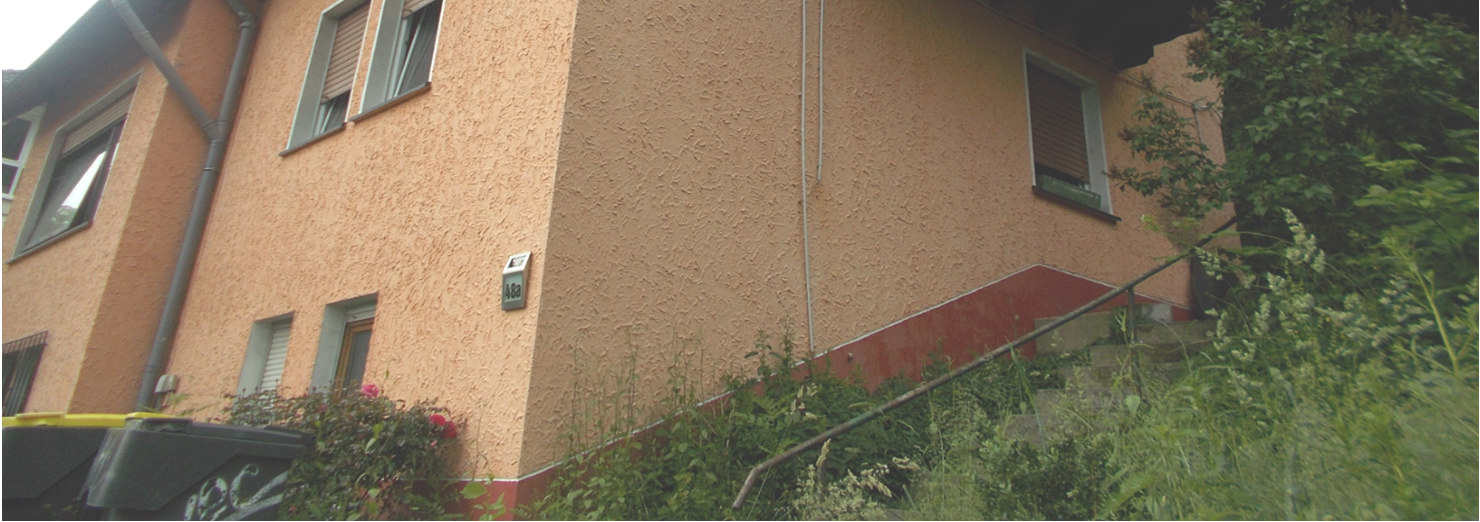 Seitenansicht eines Einfamilienhauses mit orangefarbener Fassade, Fenstern und Vegetation im Vordergrund, Hausnummer 48a in Plettenberg