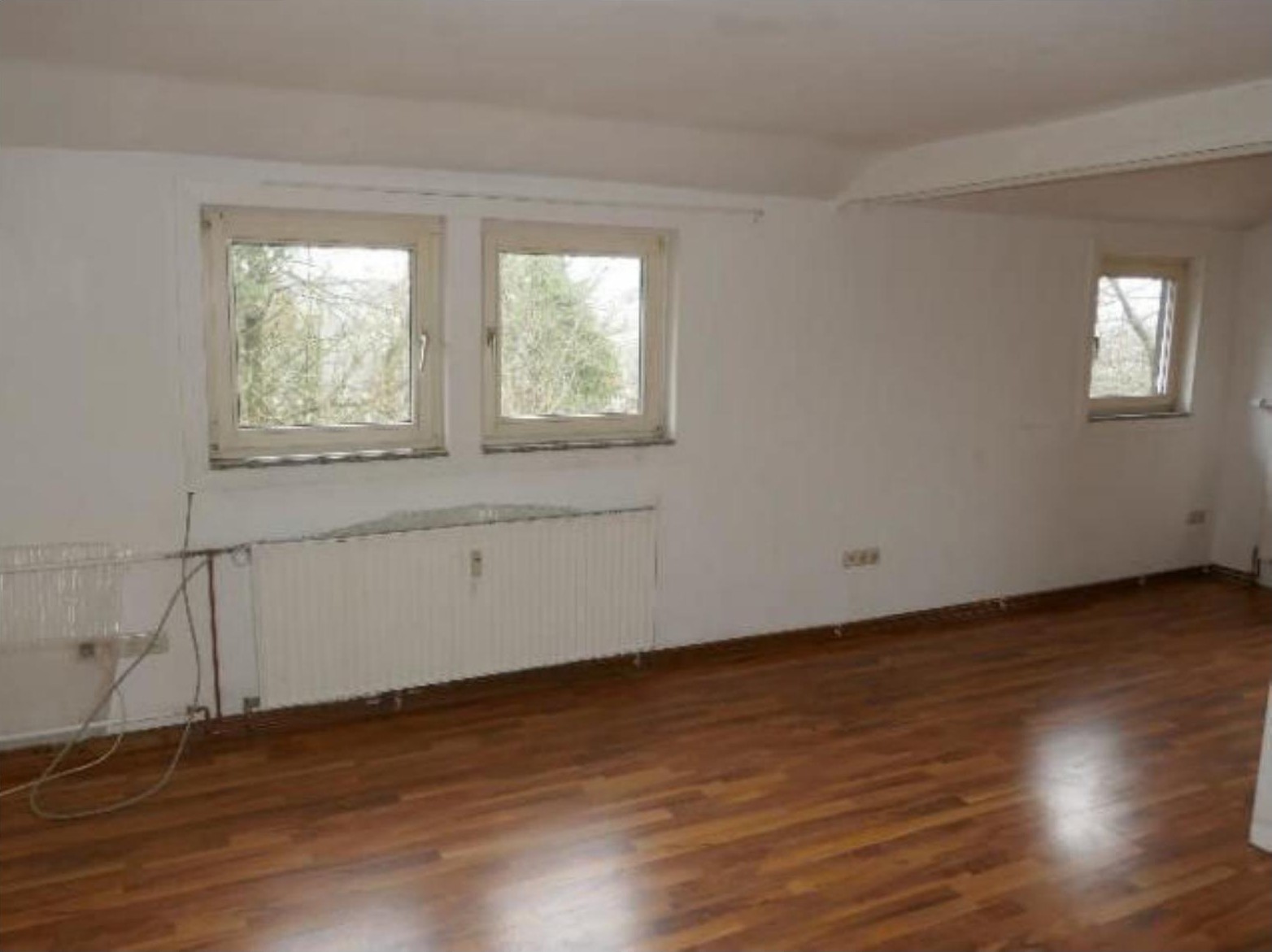 Leerer Raum mit Holzboden, weißen Wänden und Fenstern im Wohnbereich eines Gebäudes in Bad König