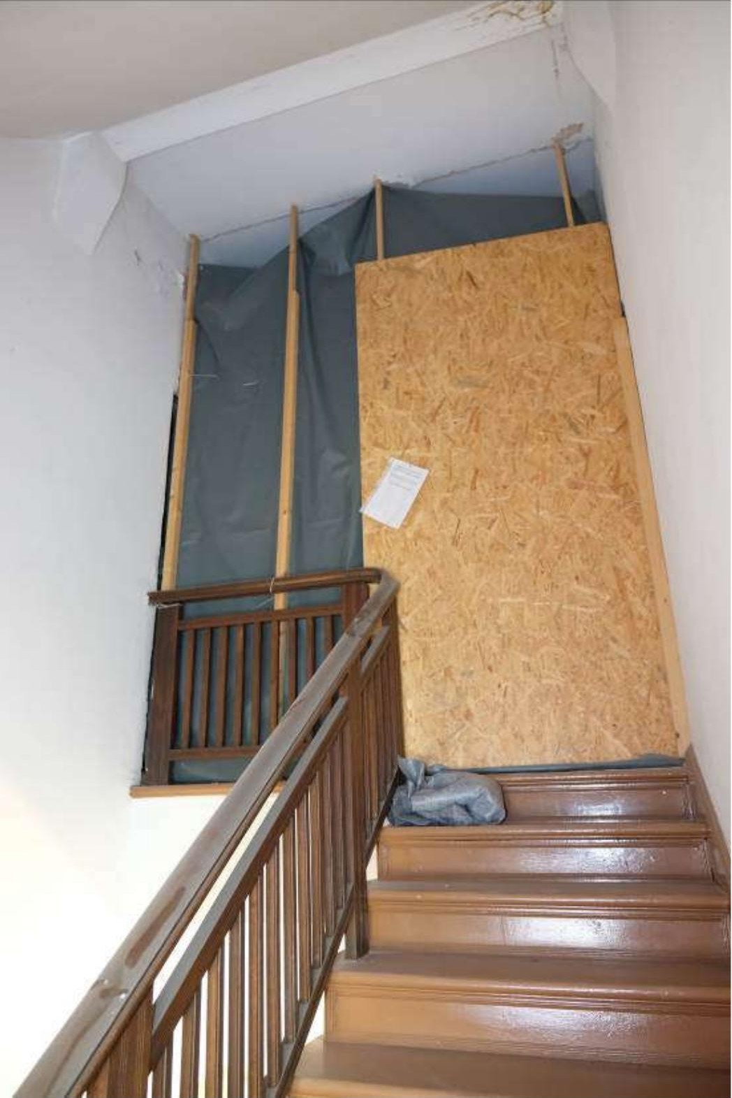 Treppenhaus mit Holztreppe und Geländer, oberer Bereich teilweise mit Sperrholz und Schutzfolie abgedeckt