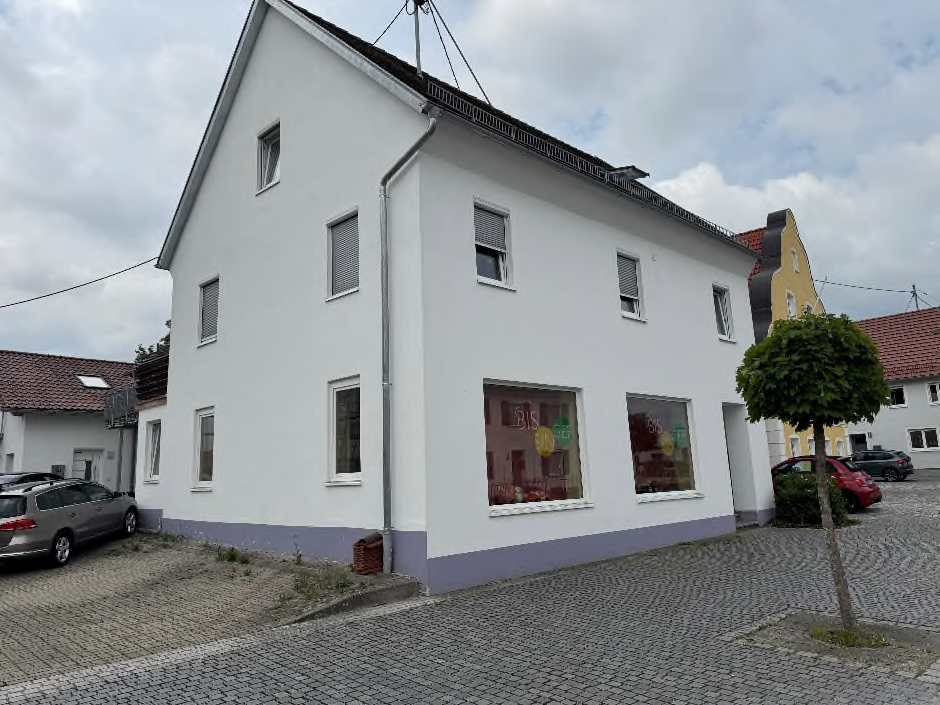 Weißes zweigeschossiges Haus mit rotem Dach an einer Kopfsteinpflasterstraße