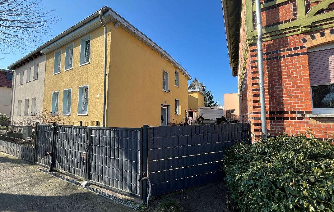 Gelbes Einfamilienhaus an der Karlstraße 5 mit dunklem Zaun und Grünbusch