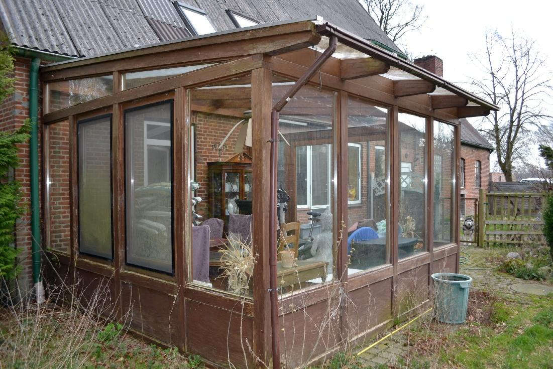 Seitenansicht eines Holz-Verandas mit Glaswänden an einem Backsteinhaus, Garten im Vordergrund