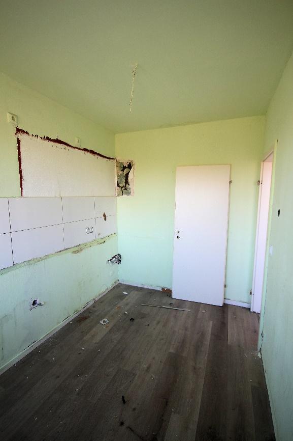 Innenraum einer Wohnung mit abgebrochenen Fliesen, sichtbaren Leitungen und Holzboden, im Zustand der Sanierung