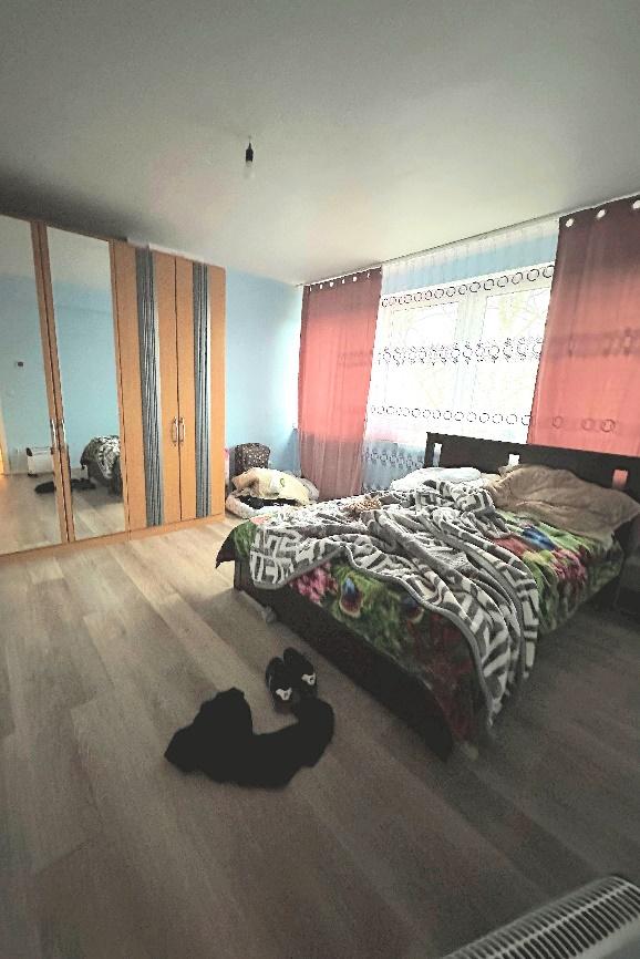 Schlafzimmer mit Doppelbett, Holzfußboden, Schrank mit Spiegeltüren und Fenster mit rosa Vorhängen