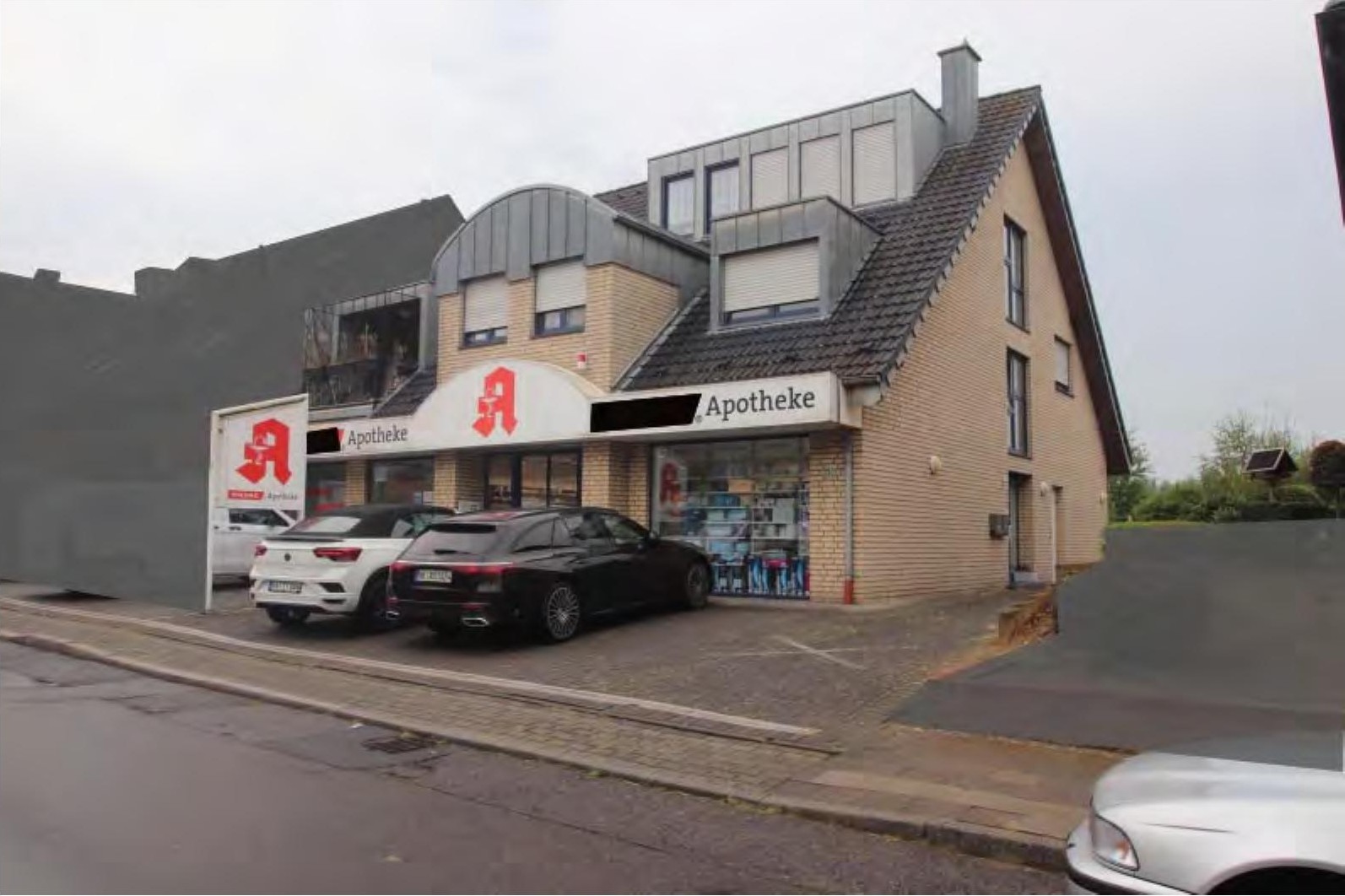 Außenansicht vorne eines Wohn-/Geschäftshauses mit Apotheke in Jüchen, Bedburdycker Straße 59, mit geparkten Autos vor dem Eingang
