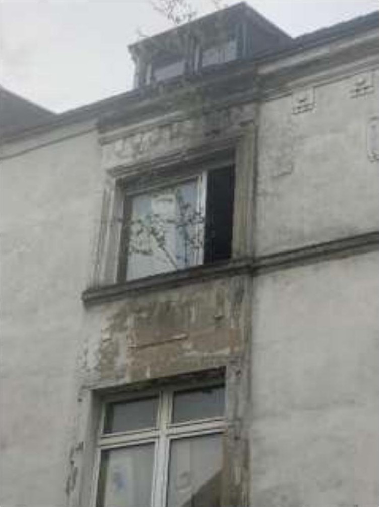 Außenansicht der Seitenfassade eines Gebäudes mit Fenstern und Dachgaube, sichtbare Verwitterungsspuren