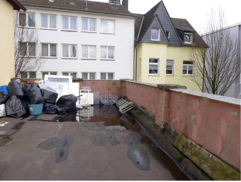Hinterhofbereich eines Mehrfamilienhauses mit Mauer, Müllsäcken und benachbarten Gebäuden in Leverkusen