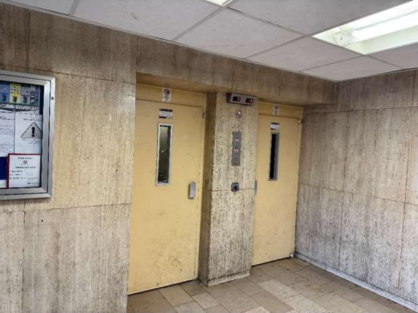 Innenraum mit zwei gelben Aufzugstüren, Betonwänden und Fliesenboden in einer Eigentumswohnung in Duisburg
