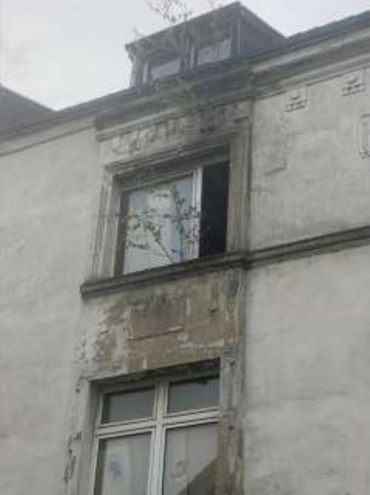 Außenansicht der Seitenfassade eines Gebäudes mit Fenstern und Dachgaube, leicht verschwommen und mit geringer Kontraststärke