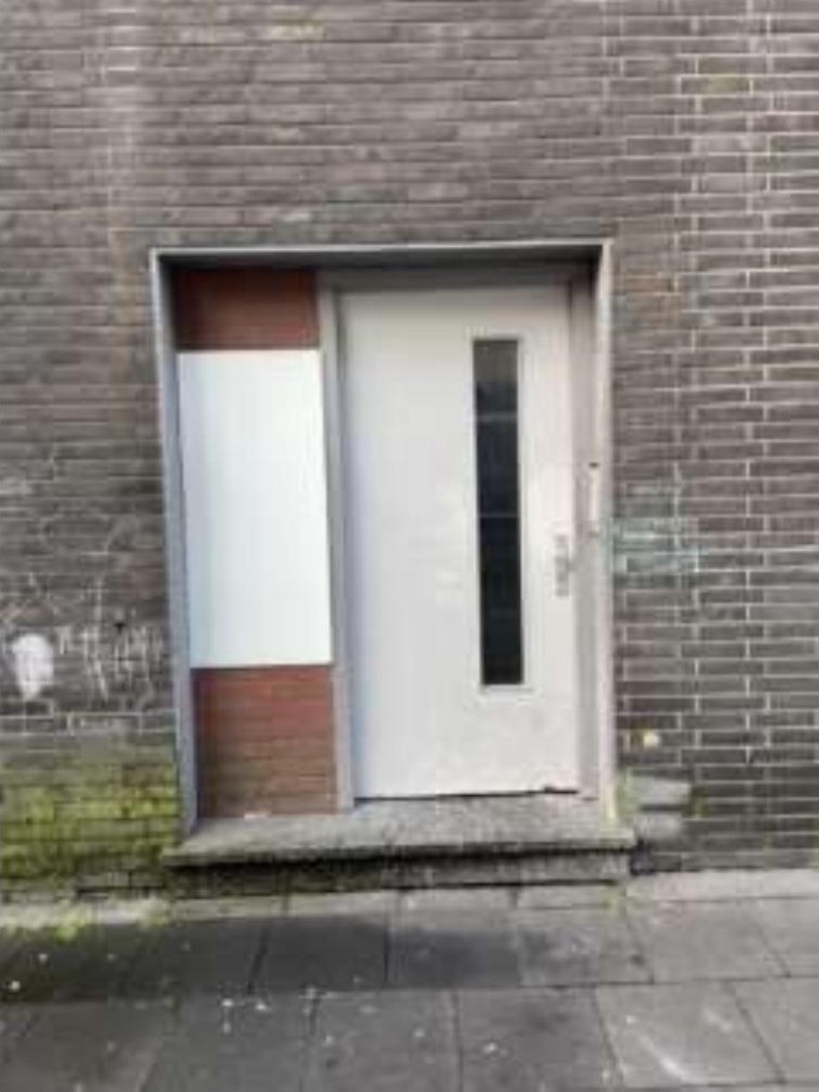 Eingangsbereich eines Gebäudes mit weißer Tür, grauer Ziegelwand und beigefarbener Seitenverkleidung in Duisburg