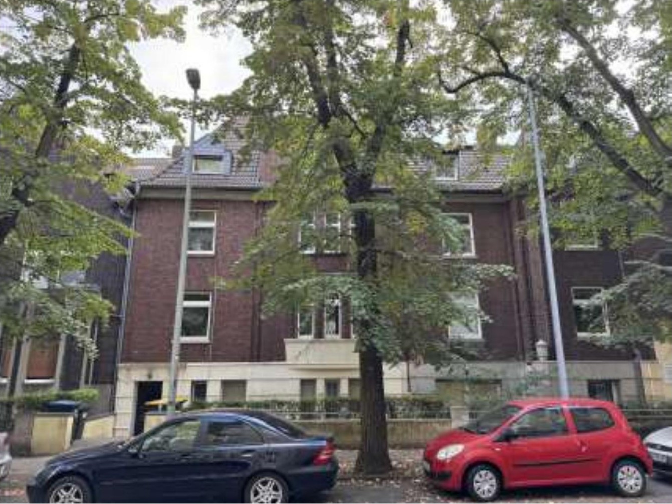 Vorderansicht eines Mehrfamilienhauses in Duisburg, Elsa-Brandström-Str. 13, mit Bäumen und geparkten Autos vor dem Gebäude