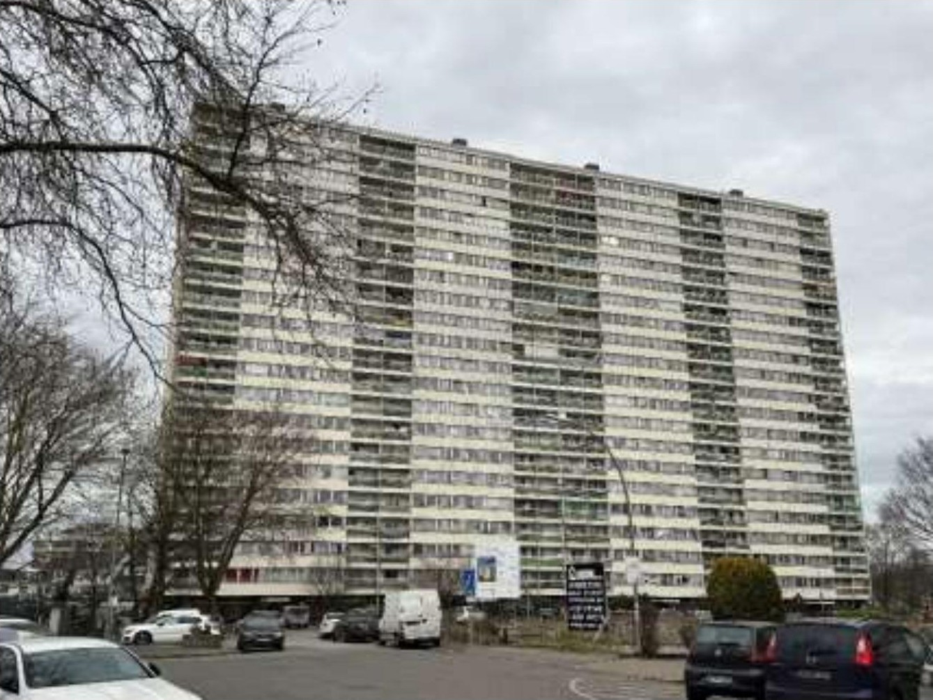 Vorderansicht eines Hochhauses mit vielen Fenstern und Balkonen, umgeben von Bäumen und Parkplätzen in Duisburg