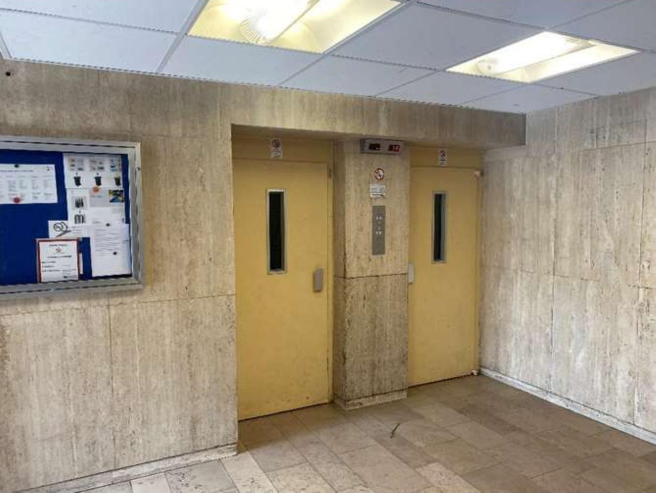 Elevatorlobby mit zwei gelben Türen, Fliesenwänden und einer Mitteilungstafel im Innenbereich der Eigentumswohnung Ottostraße 58, Duisburg