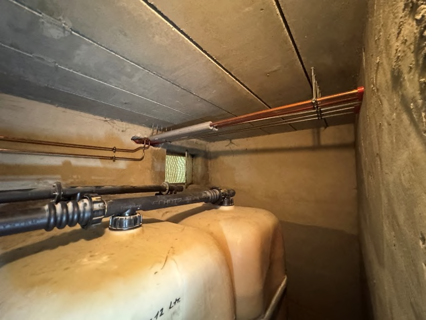 Keller mit Betonwänden, Rohrleitungen und zwei großen Behältern, vermutlich für Heizung oder Wasser