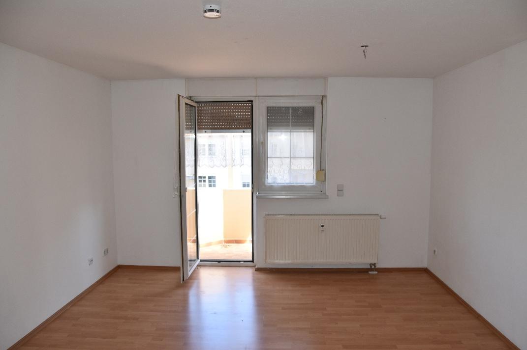 Leerer Wohnraum mit Holzboden, weiß gestrichenen Wänden, Heizkörper und Glastür zum Balkon, Eigentumswohnung in Meuselwitz