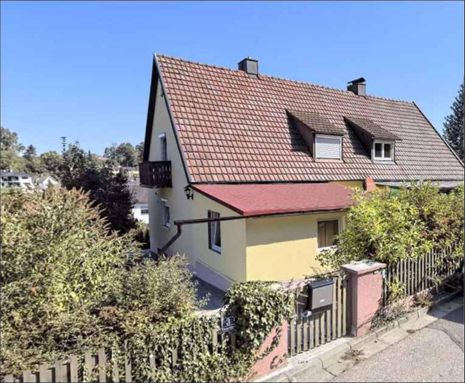 Einfamilienhaus mit Satteldach und gelber Fassade, Vorderansicht mit Balkon und Eingangstor, umgeben von Grünanlagen, Waldstraße 3, Ergoldsbach