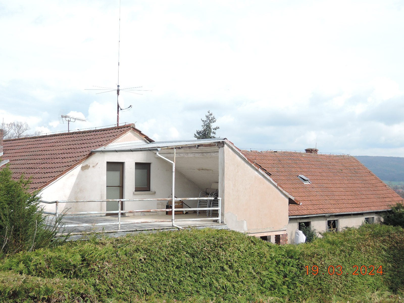 Außenansicht einer Garage mit offener Abstellfläche, Metallgeländer und Dachziegeln, umgeben von Grünanlagen