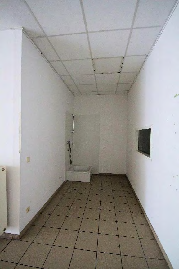 Badezimmer mit Fliesenboden, Dusche und kleinem Fenster in einer Gewerbeeinheit