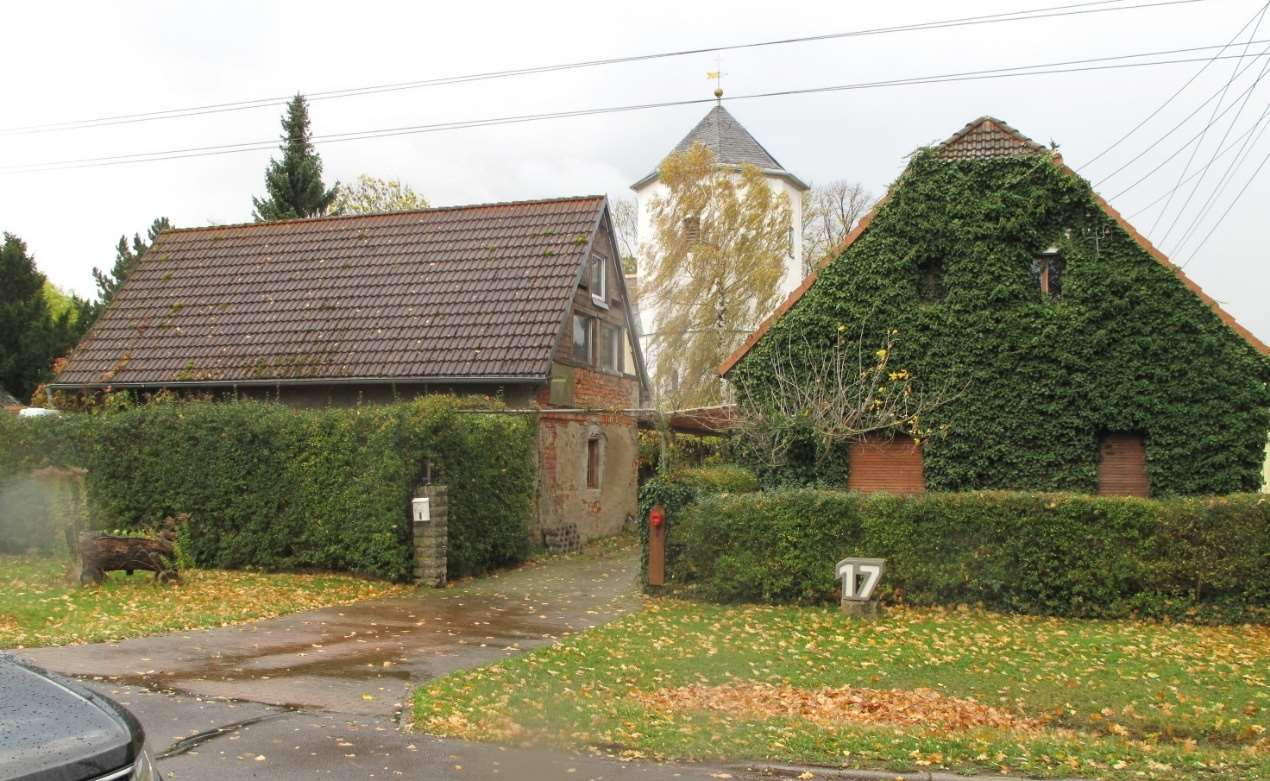 Vorderansicht eines Grundstücks mit Haus Nr. 17, umgeben von Hecken und weiteren Gebäuden, im Herbst mit Laub auf dem Boden