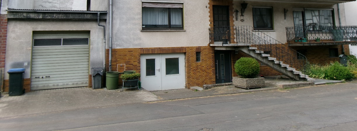 Fassade eines Mehrfamilienhauses mit Garagenzugang, Eingangstüren, Fenstern und Außentreppe in Breitenbach a.H