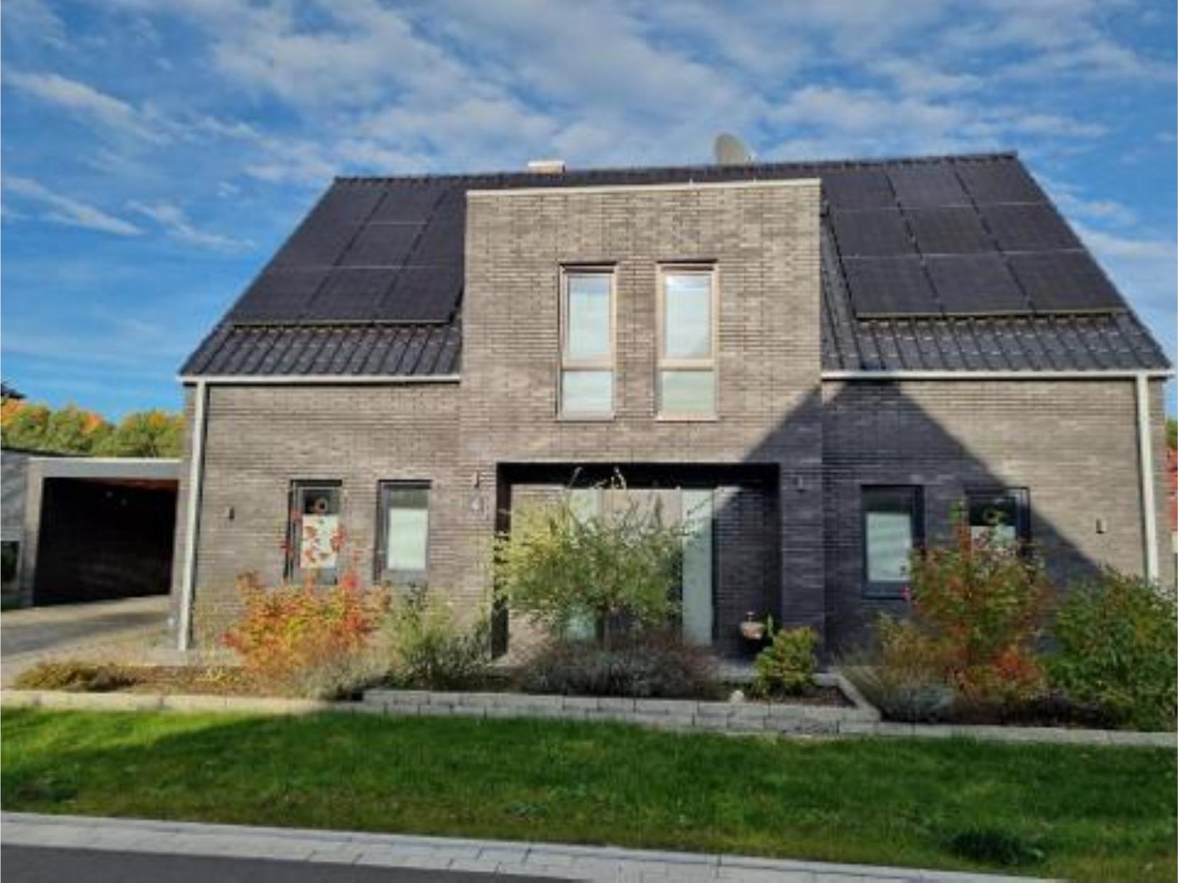 Einfamilienhaus mit grauer Fassade und Solaranlage auf dem Dach, Vorgarten mit Grünflächen und Pflanzen, Eingangsbereich im Zentrum