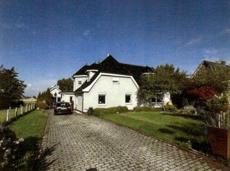 Einfamilienhaus mit dunklem Dach und weißer Fassade, gepflasterter Einfahrt, grüner Vorgarten, geparktem Auto, Simonsberg, Rieke Reech 61