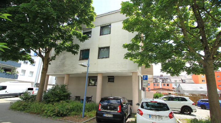 Parkplatz vor einem mehrstöckigen Gebäude in der Arnulfstr. 12, 89231 Neu-Ulm, mit geparkten Fahrzeugen und Bäumen im Vordergrund