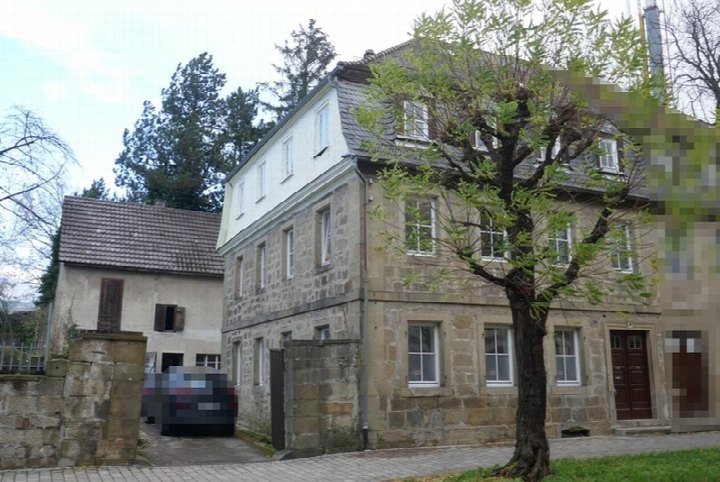 Fassade eines mehrstöckigen Steinhauses in Öhringen, Karlsvorstadt 35, mit grauem Satteldach, Fenstern und Eingangstür; vorne Baum und gepflasterter Hof