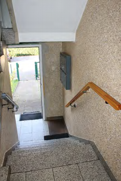 Treppenhaus mit Granitstufen, Holzgeländer und Eingangstür zur Außentreppe