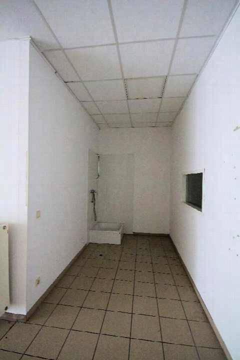 Badezimmer mit Fliesenboden, Dusche und kleinem Fenster in einer Gewerbeeinheit