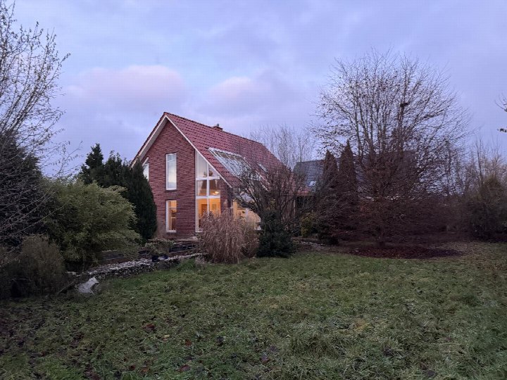 Einfamilienhaus mit rotem Ziegeldach und großen Fenstern, Seitenansicht mit Garten und Bäumen im Vordergrund, Wiesmoor, Marderweg 40