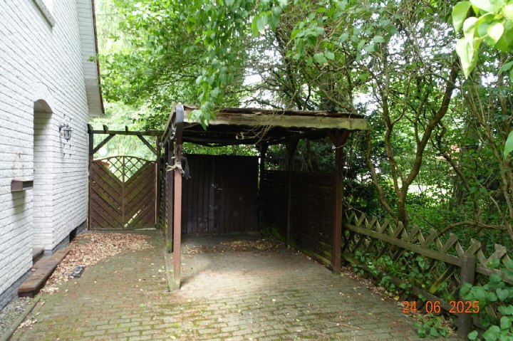 Gartenbereich mit Pergola, Holztor und Bepflanzung neben einem weißen Backsteinhaus