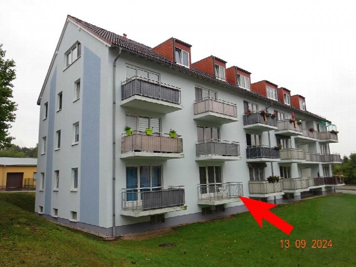 Seitenansicht eines mehrstöckigen Wohngebäudes mit Balkonen, Fenstern und Dachgauben auf einem Grünstreifen