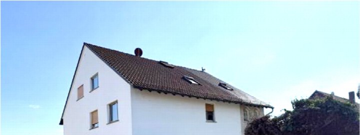 Seitenansicht eines weißen Gebäudes mit braunem Ziegeldach, mehreren Fenstern und Dachfenstern unter klarem Himmel