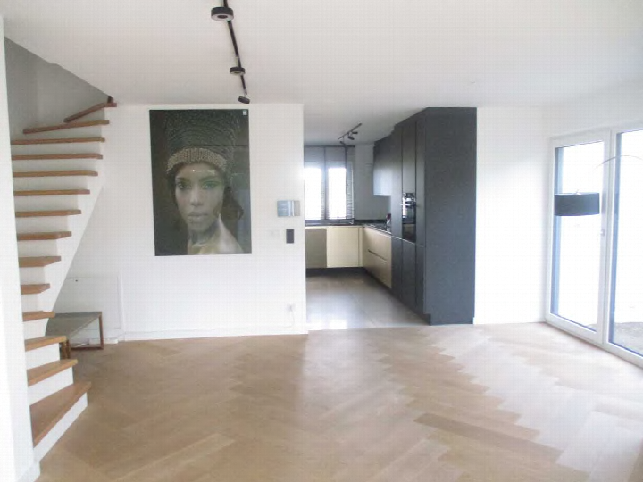 Geräumiger Wohnbereich mit Holzboden, Treppe und Blick in die Küche. An der Wand hängt ein großes Porträt