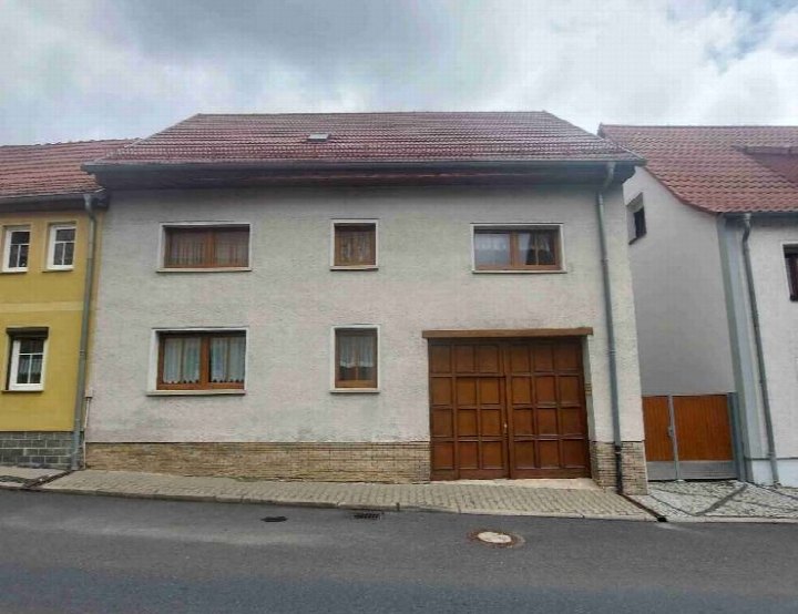 Fassade eines zweistöckigen Einfamilienhauses mit rotem Ziegeldach, Holztür und Fenstern an der Karl-Marx-Straße 7 in Weißensee