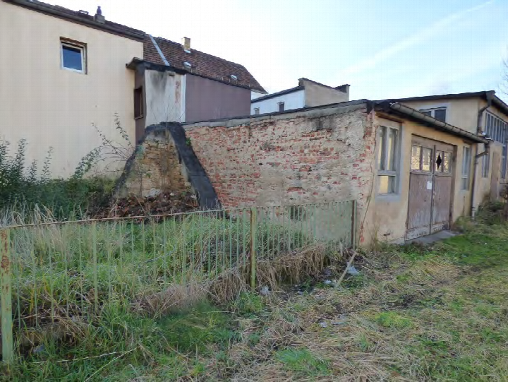 Überwuchertes Grundstück mit Metallzaun, verfallener Mauer und angrenzenden Gebäuden in Freital, Zur Lessingschule