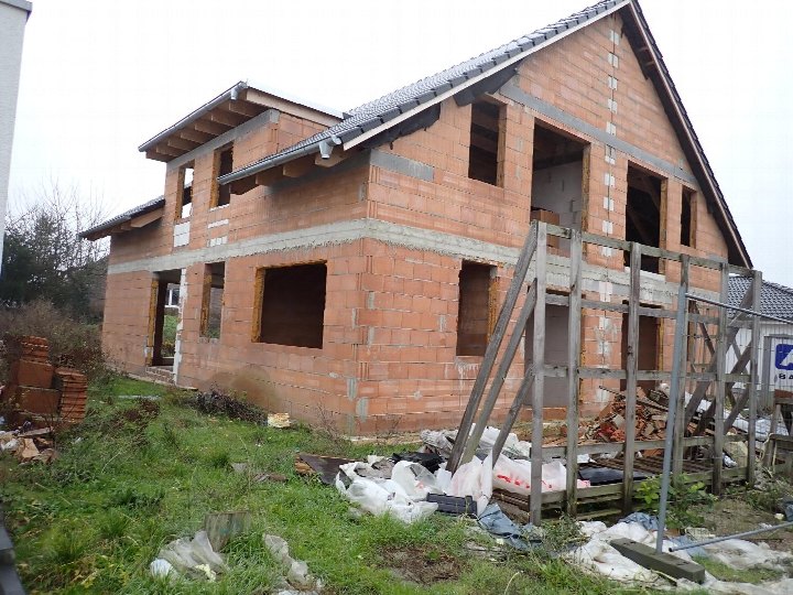 Zweistöckiges Haus in Rohbau mit roten Ziegeln, Dach und Fensteröffnungen, Baustellenaufnahme von vorne