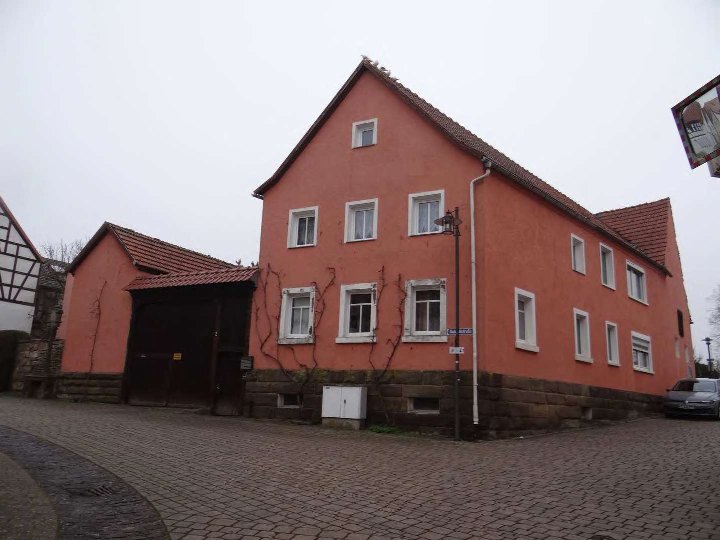 Rotes Einfamilienhaus mit Satteldach und Steinsockel, Eingangsbereich mit Garage, Schloßstraße 2, Ebenhausen